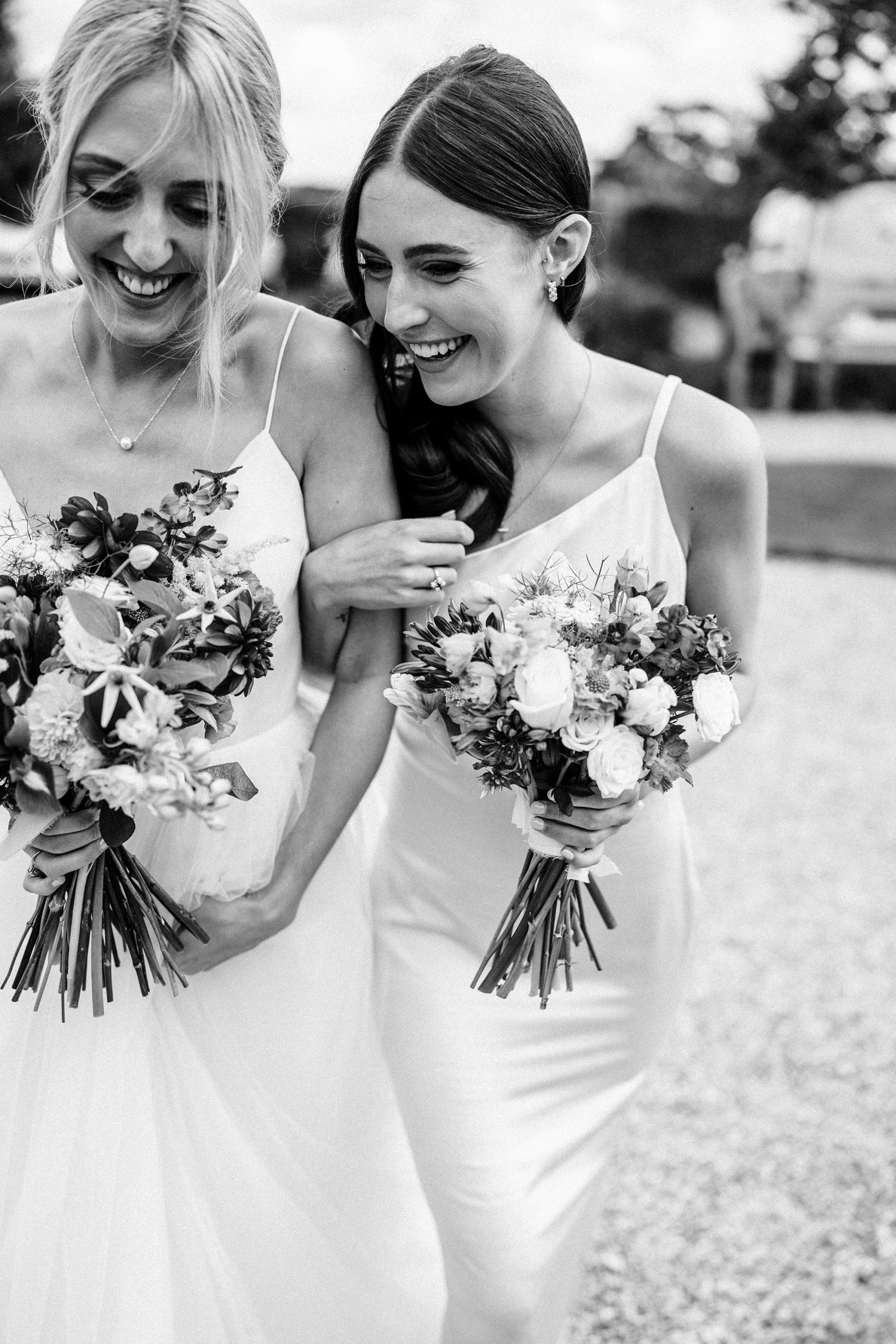 Bride and bridesmaid share a joke clasping their bouquets.