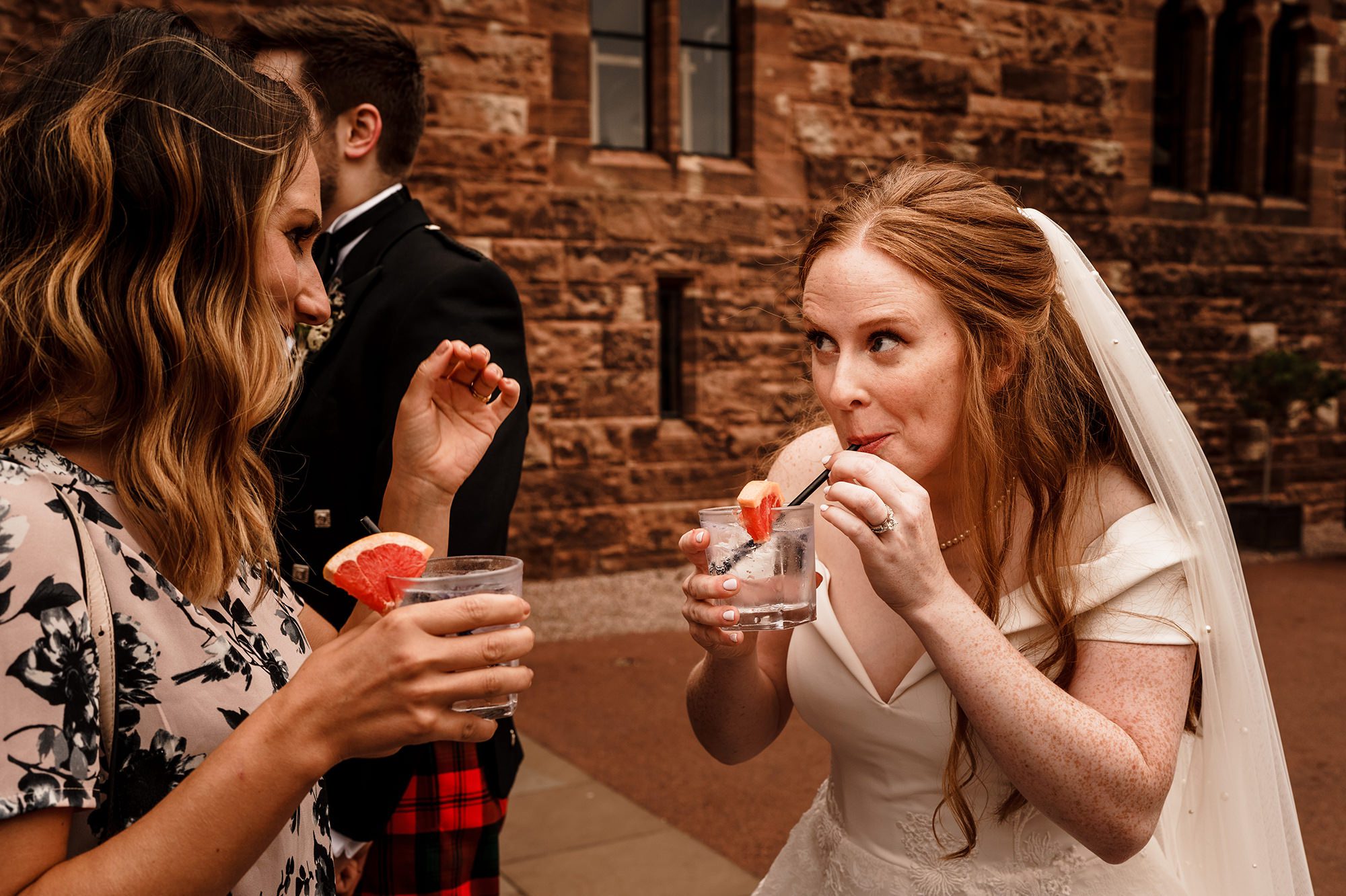 bride takes a drink of her cocktail whilst taking to a guest