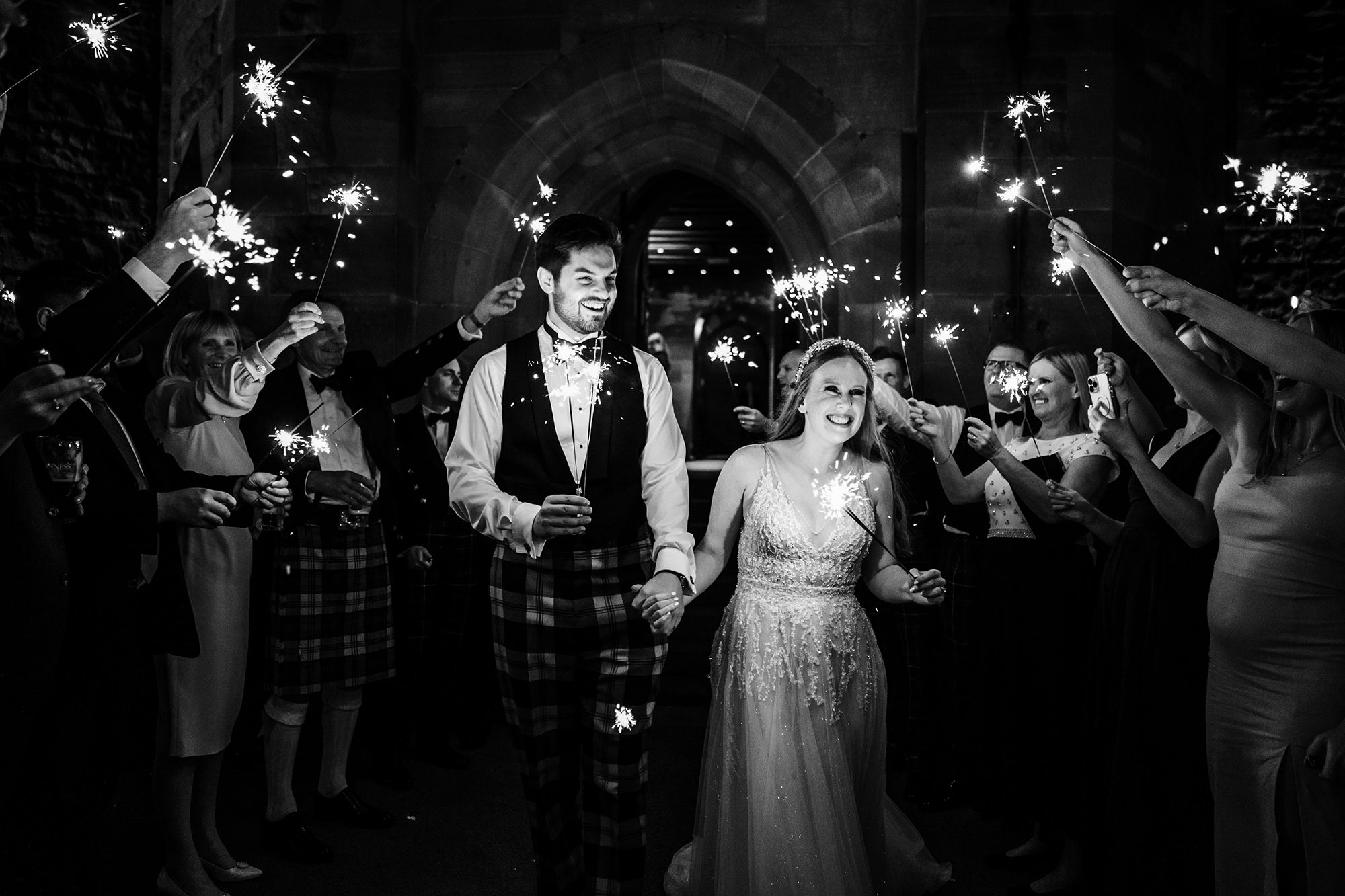 bride and groom hold sparklers outside Peckforton Castle on their wedding day