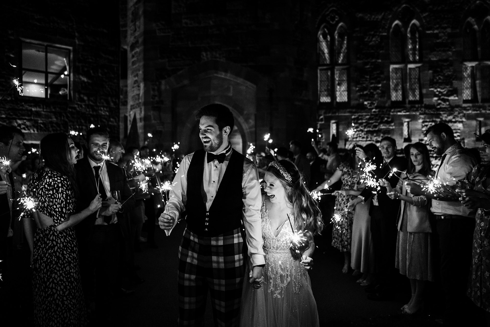 bride and groom smiling and holding sparklers in the dark at their wedding