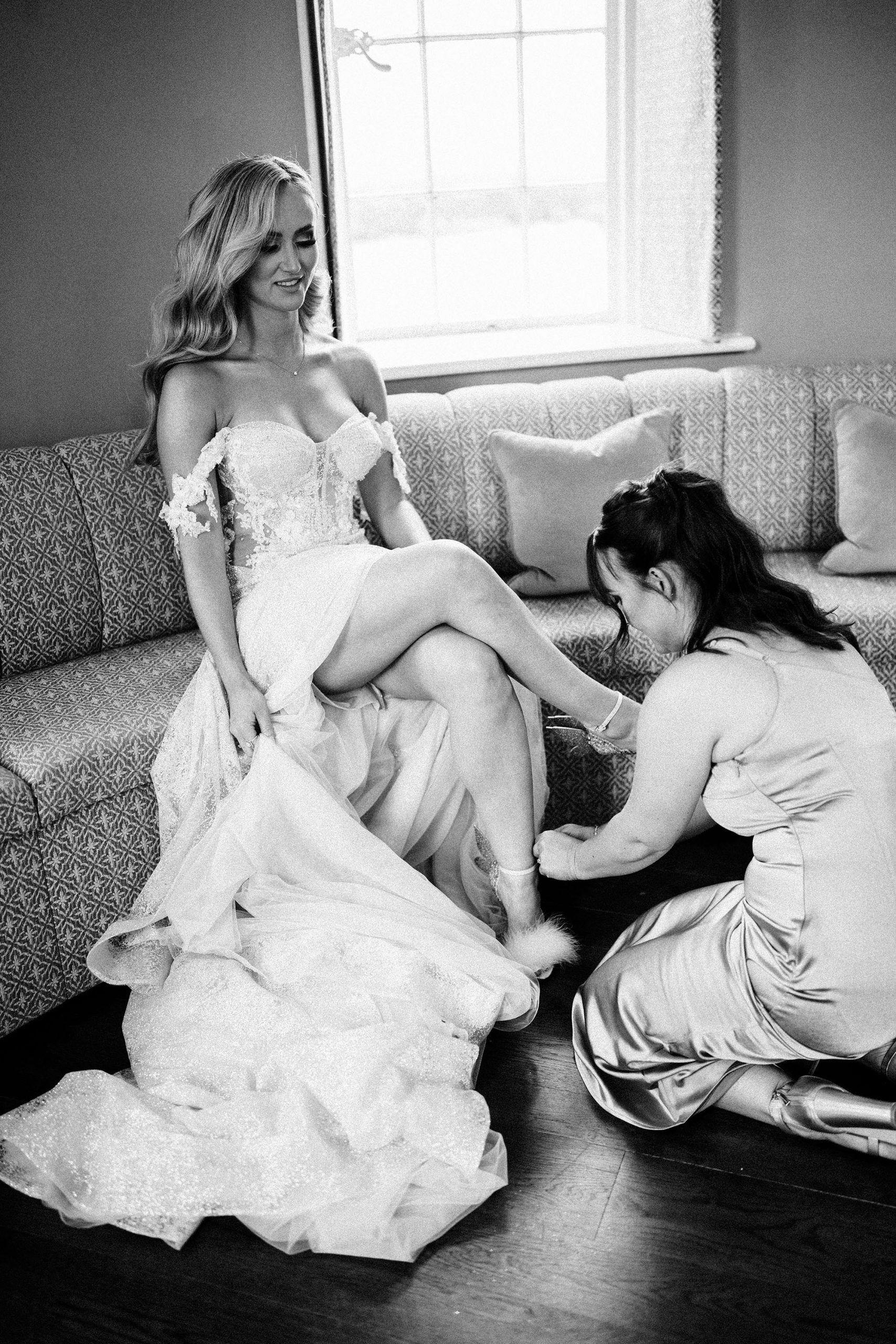 bridesmaid putting shoes on bride at Hawkstone Hall